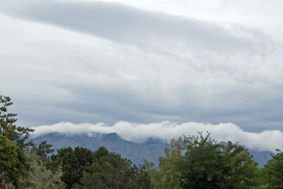 A photo of clouds spilling over the tops of the Sandia Mountains.