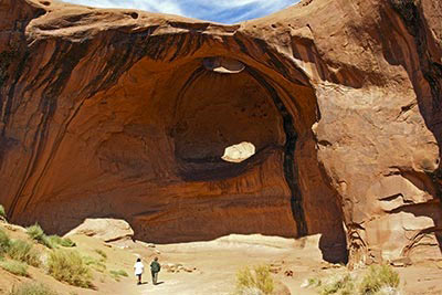 A photographic image of Charlene, our tour guide, and Mary Hunt Webb approaching a large cavity in a rock formation in Monument Valley, Arizona.