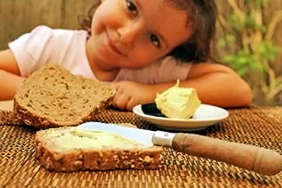 A photographic image of a girl eating bread and butter.