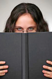 A photographic image of a woman peering over the top of a book.