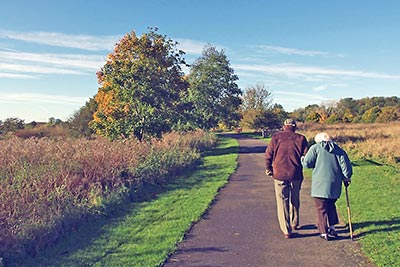 A photographic image of an elderly couple walking on a country path.