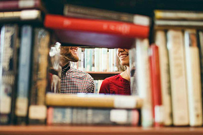 A photograpic image of couple flirting among a stack of books.