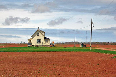 A photographic image of an empty field with a farmhouse.