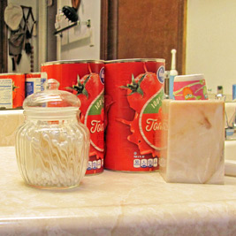 A photographic image of two large cans of tomato juice next to a hair dryer and a shower cap.