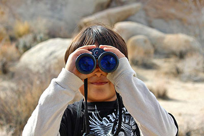 A photographic image of a boy spying through binoculars.