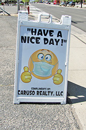 A photographic image of a real estate sign that contains a smiley face wearing a mask.