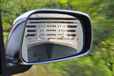 A photographic image of a ship in a rearview mirror.
