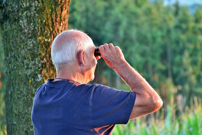 A photographic image of a senior man with binoculars.