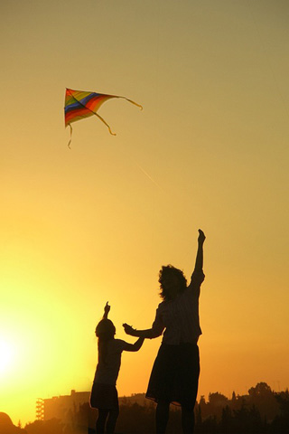 A photographic image of a mother and son flying a kite towards sunset.