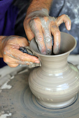 A photographic image of a potter forming a vase with his hands.